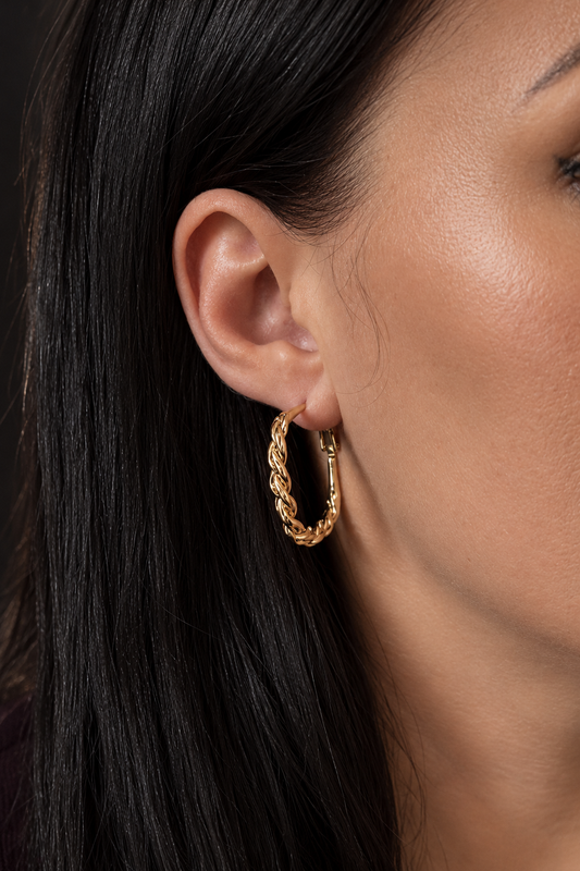 Apzeltīts vīts riņķu auskars modeles ausī, silts zelta tonis